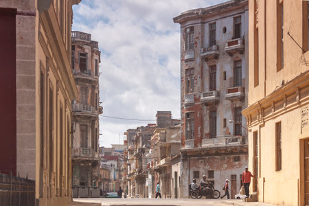 Havana, Cuba - March 23, 2010: A sidecar motorcycle and several people cross along a typical street with old and in poor condition buildings, in the central area of Havana, not far from the Malecon.のeditorial素材