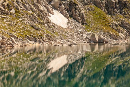 Crystalline reflections on the clean and turquoise water of a high-altitude lake, of the silent mountains in summer, in the Aragonese Pyrenees, Huesca, in the area of the Posets-Maladeta Natural Park.の写真素材