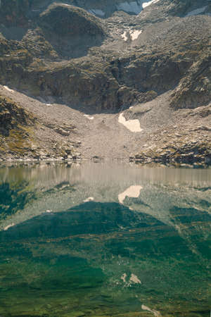 Crystalline reflections on the clean and turquoise water of a high-altitude lake, of the silent mountains in summer, in the Aragonese Pyrenees, Huesca, in the area of the Posets-Maladeta Natural Park.の写真素材