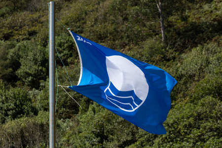 San Pedro de la Ribera, Spain - August 16, 2020: Blue flag of FEE, European Foundation for Environmental Education, fluttering in the wind on a beach in Asturias, on a hot summer day.のeditorial素材