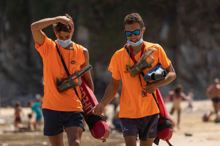 San Pedro de la Ribera, Spain - August 16, 2020: A couple of lifeguards from the public security services walk with the protective face mask on a beach in Asturias, in the middle of summer.のeditorial素材