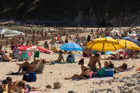 San Pedro de la Ribera, Spain - August 16, 2020: Beach in Asturias, full of bathers, umbrellas, tourists and local inhabitants on a summer day, enjoying the sand, the sea and the natural environment.のeditorial素材