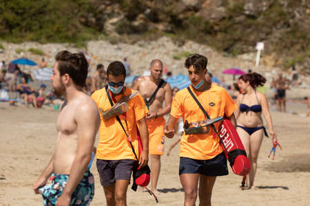 San Pedro de la Ribera, Spain - August 16, 2020: A couple of lifeguards from the public security services walk with the protective face mask on a beach in Asturias, in the middle of summer.のeditorial素材