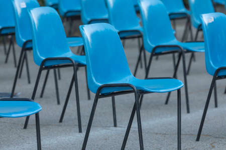 Rows and columns of nondescript blue plastic chairs, consecutive, arranged in a line, at similar...