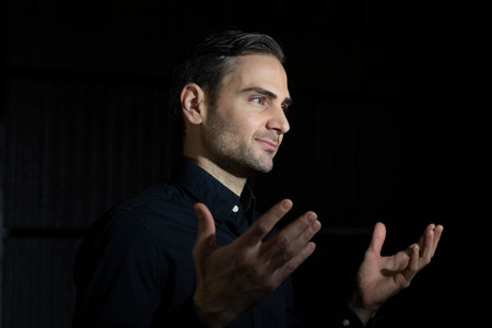 An influencer, artist and musician, dress with black shirt, poses for the camera in one of his photographic shootings for social networks, in a dark backstage area, at night, in Spain.の写真素材