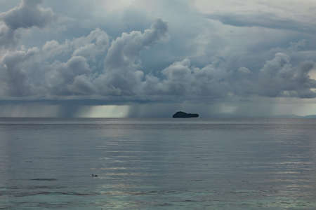 Huge storm clouds on a rainy day, over the horizon and one of the small islands of Friwin, passing through the Raja Ampat, West Papua, Indonesiaの写真素材