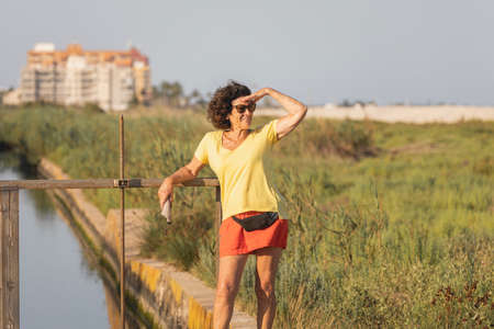 A cheerful and vital woman, in her 70s, observe the landscape around her, next to a natural beach, at sunset, in the Mediterranean Sea, Spainの写真素材