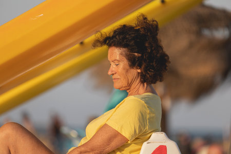 An adult woman, in her 70s, sitting quietly on the beach, thinking and meditating, while sunbathing, Mediterranean, Spainの写真素材