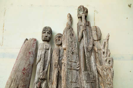 Waisai, Indonesia - Oct 16, 2019: Old tribal looking wooden carved figurines lie abandoned against the side of an old houseのeditorial素材