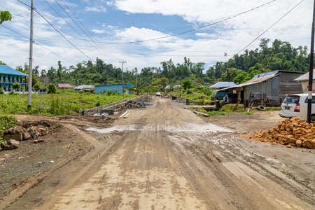 Waisai, Indonesia - Oct 16, 2019: One of the main streets leading to the port of Waisai, full of wet mud and some puddles on a sunny dayのeditorial素材