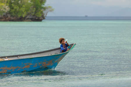 Friwin, Indonesia - Oct 14, 2019: A little boy travels in the bow of a motor boat, Raja Ampat, West Papuaのeditorial素材