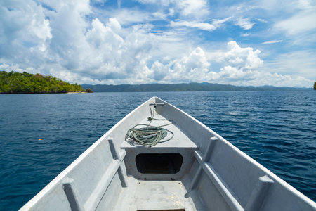 Bow of a motor boat plowing through the blue waters between the islands of Friwin and Gam on a sunny...