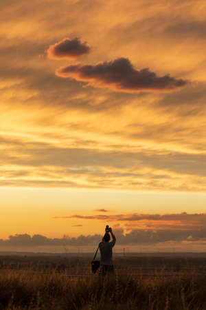 The silhouette of a young man taking pictures of the clouds, dwarfed by the landscape at sunset, in Gallur, Aragon, Spainの写真素材