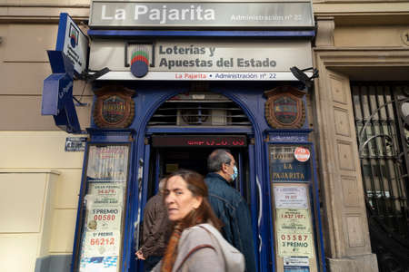 Madrid, Spain - Nov 09, 2021: A woman crosses fast in front of the Administration of lotteries and bets of the state number 22, La Pajarita, in Alcala streetのeditorial素材