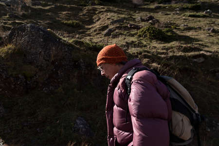 A mountaineer, senior adult man, in his 70s, wearing a feather coat and sunglasses, enjoys a hike up...
