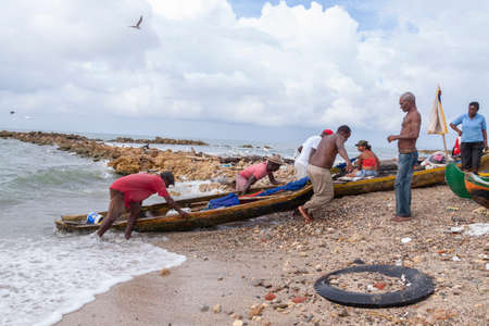 Cartagena de Indias, Colombia - Nov 23, 2010: A group of poor fishermen struggle to drag a boat out of the water on one of the rocky beaches near the city, in the Colombian Caribbeanのeditorial素材