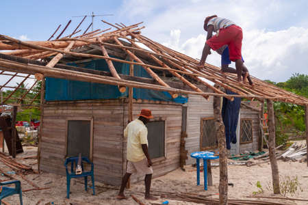 Cartagena de Indias, Colombia - Nov 22, 2010: A group of men repair the roof of a humble wooden house, broken after a storm, on the beach of Isla Baru, in the Colombian Caribbeanのeditorial素材