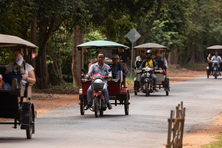Angkor, Cambodia - Nov 24, 2019: Several tuk tuk, or rickshaw, transit, taking tourists, along one of the roads that run through Angkor Wat, in the Angkor Archaeological Park, Siem Reapのeditorial素材