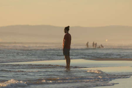 Zahara de los Atunes, Spain - Sept 03, 2021: A young man pensively observes the water and waves on the beach, at sunset, Cadiz provinceのeditorial素材