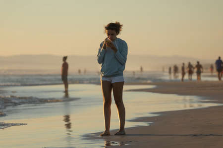 Zahara de los Atunes, Spain - Sept 03, 2021: A young adolescent girl looks at the mobile phone on the beach, at sunset, Cadiz provinceのeditorial素材