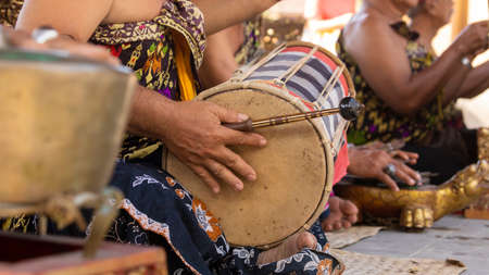 A musician plays a kendhang or ketipung, a traditional Balinese instrument, as part of a musical ensemble or gamelan, during a performanceの写真素材