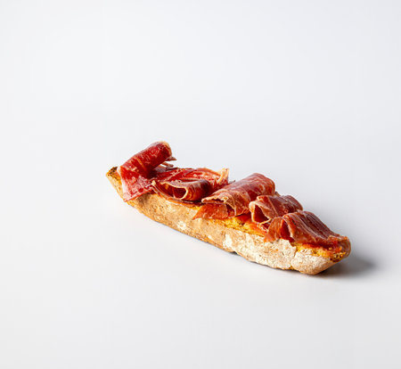 A toast of bread with olive oil and natural tomato, with cured serrano ham iberico, on a white backgroundの写真素材