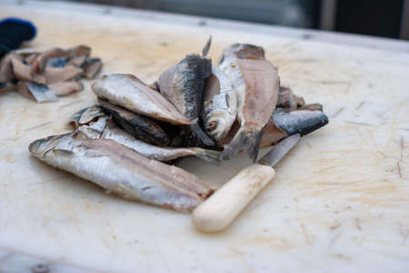 Small fish next to white handled knife on white cutting boardの写真素材