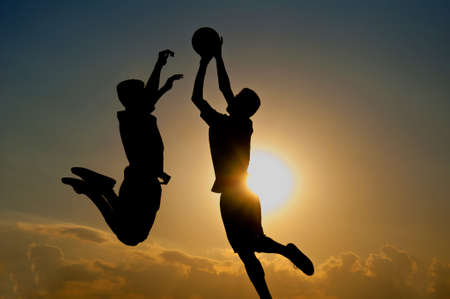 silhouette of goalkeeper jumping for catch the ball in the air with sundown backgroundの写真素材