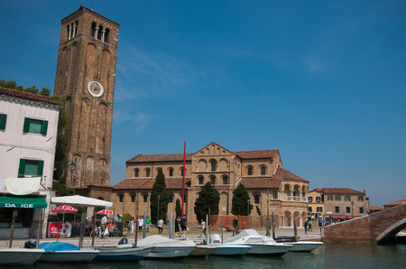 Narrow canal, church and tall belfry with clock in Murano - small island in Venetian lagoon, popular tourist destination, famous for its glass makingのeditorial素材