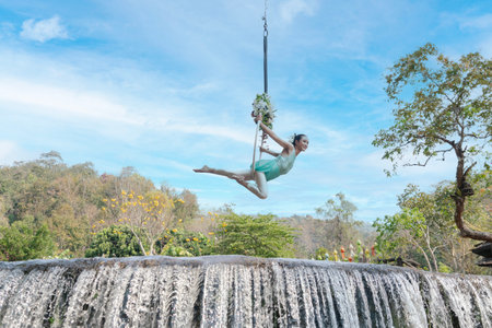Young woman swinging on a swing in a tropical jungle with a waterfall in the backgroundの写真素材