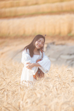 Beautiful young woman standing with violin on a barley field.の写真素材
