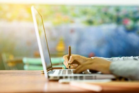 The hands of a young businesswoman signing a paper on a notebook using a pen while using a laptop computer. Business and Technology Concepts.の写真素材