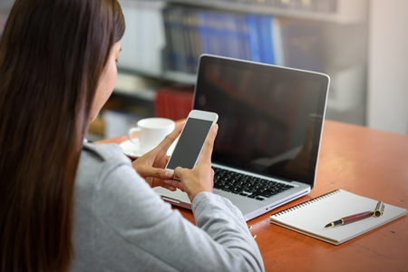 Beautiful Asian businesswoman using a mobile phone with a laptop in the office. Financial and Technology Concepts.の写真素材