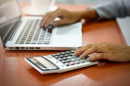The hand of Beautiful businesswoman uses a calculator in the office. With laptop computer on the wood table. Business and Technology Concepts.の写真素材