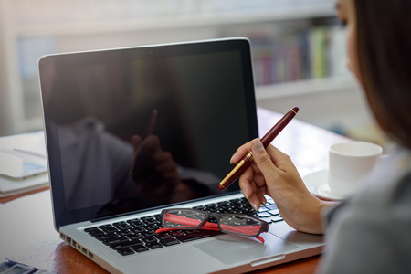 Asian Beautiful businesswoman holding a pen while using a laptop computer in her office. Finance, Banking and Technology Concepts.の写真素材
