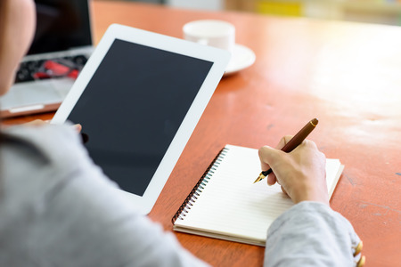 Beautiful Asian businesswoman was looking at the tablet and taking notes on her desk on the wood table in her office.  Finance, Banking and Technology Concepts.の写真素材