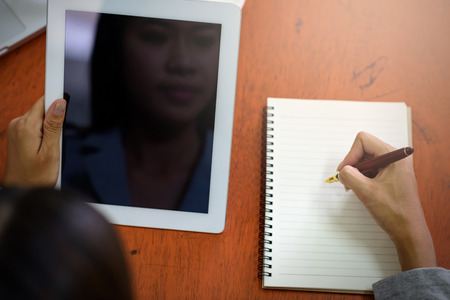 Beautiful Asian businesswoman was looking at the tablet and taking notes on her desk on the wood table in her office.  Finance, Banking and Technology Concepts.の写真素材