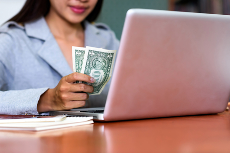 Money exchange with Asian business woman checking exchange rates through a laptop computer.の写真素材