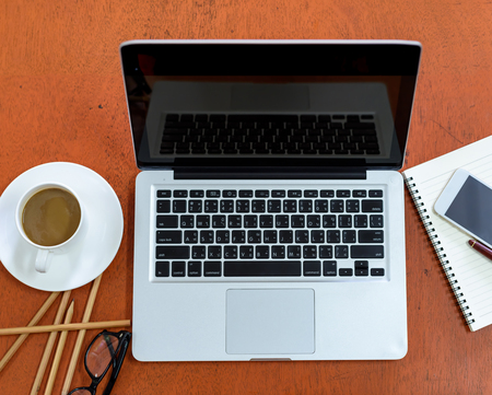white cup of coffee with a notebook computer and glasses on a wooden desk.の写真素材