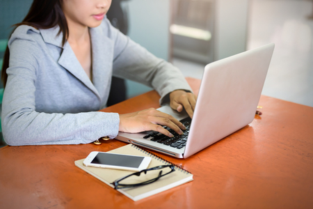 Beautiful businesswoman uses a laptop computer in the office. With the phone and notebook placed on the wood table. Business and Technology Conceptsの写真素材