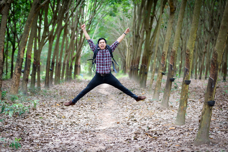 Happy Asian man backpack jump in the rubber plantation background. Travel and holiday concept.の写真素材