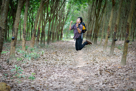 Happy Asian man backpack jump in the rubber plantation background. Travel and holiday concept.の写真素材