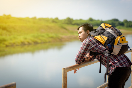 An Asian tourist man carrying backpackers is watching the river. Holidays and nature concepts.の写真素材