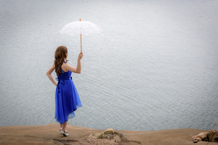Beautiful woman wear blue evening dress hold white umbrella watching the view on the rocks.の写真素材