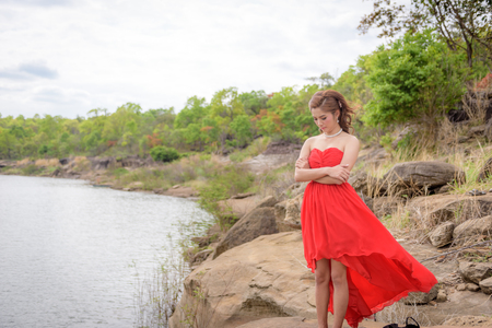 Beautiful woman wear red evening dress over mountains and rivers background.の写真素材
