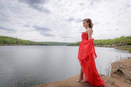 Beautiful woman wear red evening dress over mountains and rivers background.の写真素材