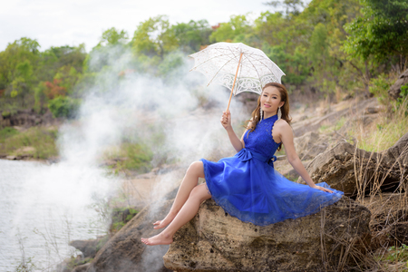 Beautiful woman wear blue evening dress hold white umbrella on the rocks.の写真素材