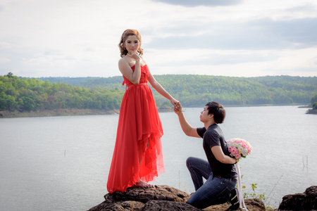 Young man hiding a bouquet of flowers behind him is about to deliver a young woman in red dress.の写真素材