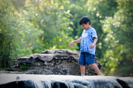 A boy standing on a rock with a waterfall in a rain forest on a mountain.の写真素材