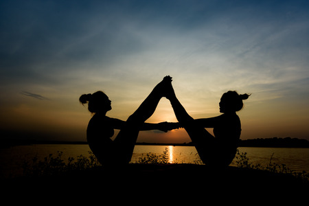 Black silhouette, beautiful mother and daughter are practicing yoga on rocks near the river. During the sunset and dusk.の写真素材